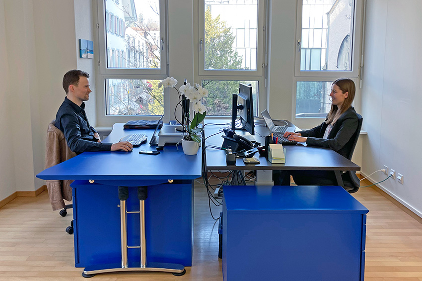 Simon Kaserer und Alina Alisauskaite sitzen einander gegenüber am Bürotisch und arbeiten